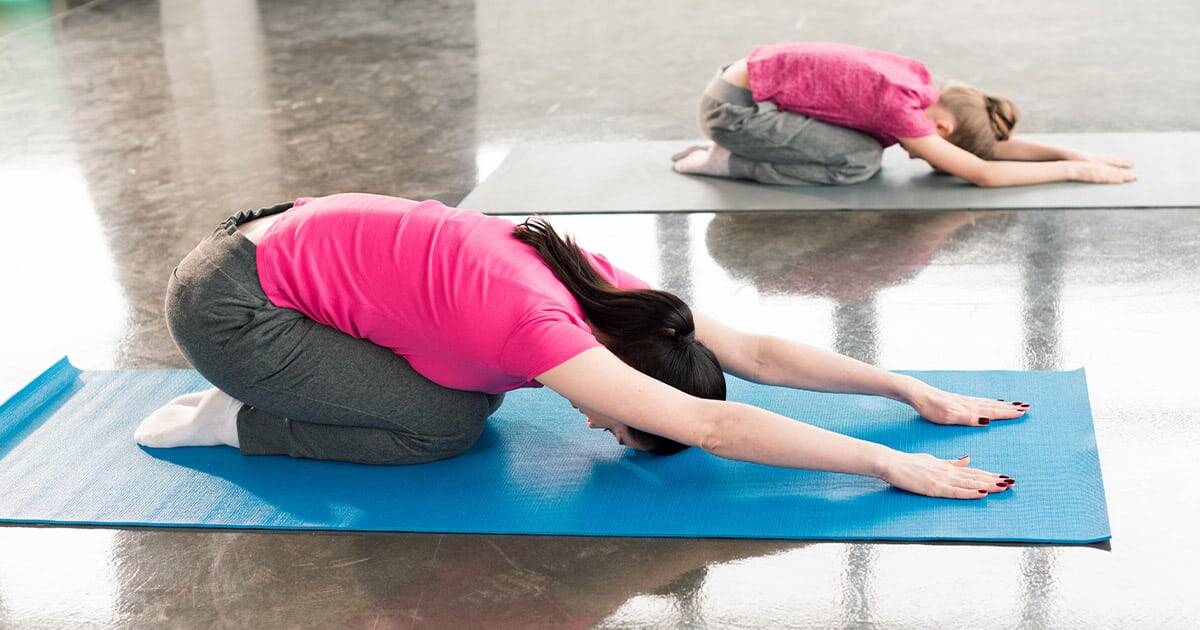 Child and adult practicing yoga in child's pose on mats for stress relief and flexibility.