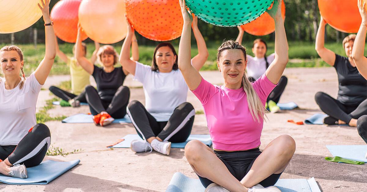 Colorful outdoor yoga session for women with exercise balls and mats.