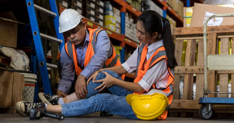 An emergency response training with a male supervisor assisting a female coworker in a warehouse environment to promote safety and injury prevention.