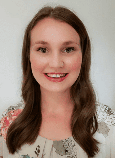 Woman smiling with long brown hair and floral top.