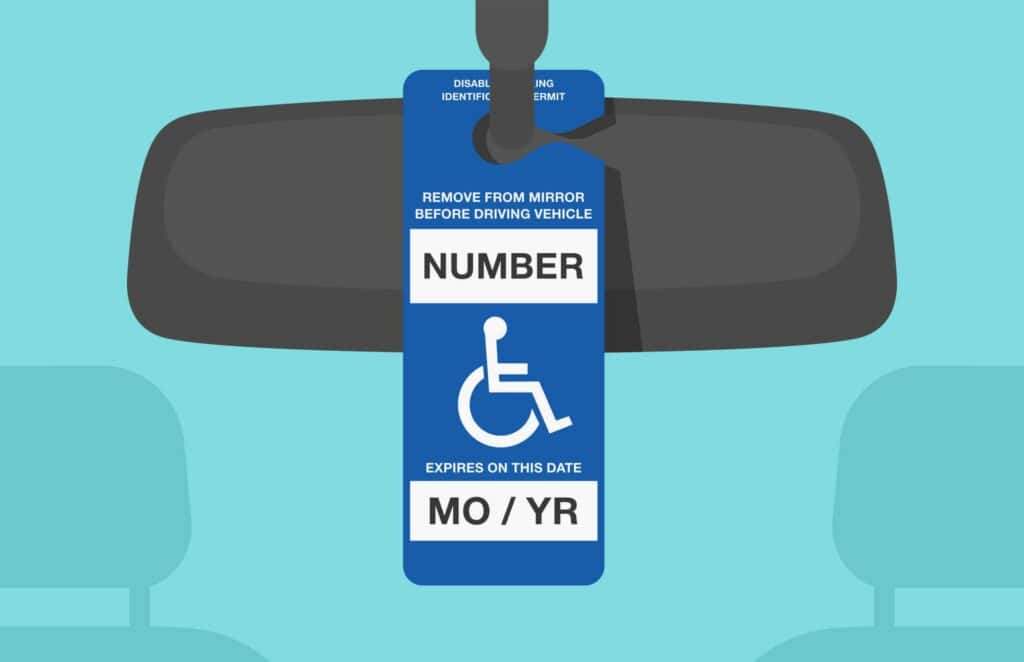 Blue disability parking placard hanging from rearview mirror in vehicle.