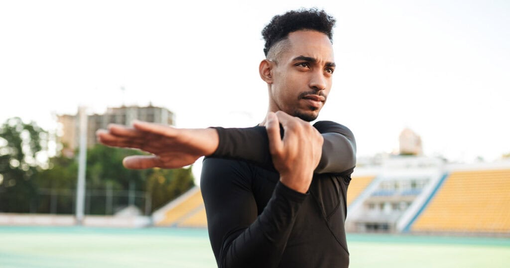 Young man stretching arm outdoors for flexibility and stress relief.