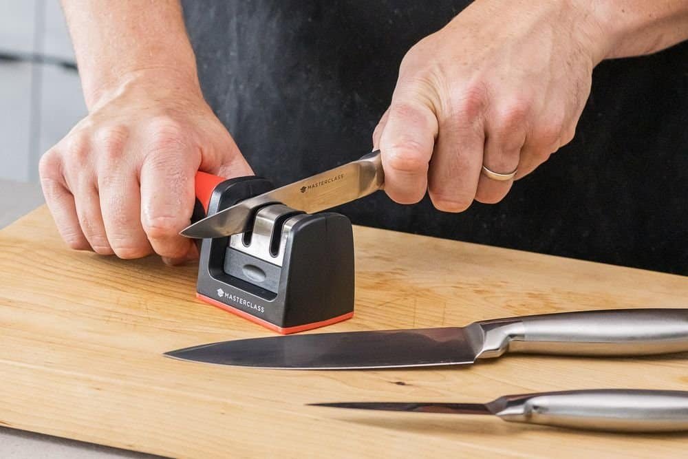 person using a manual knife sharpener to sharpen a kitchen knife on a cutting board