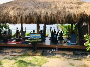 קבוצת מטיילים מתרגלים יוגה על דק עץ מול הים בשעות הבוקר - איסט קארד