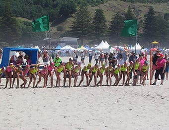 A group of surf life savers in neon uniforms lining up on the beach.