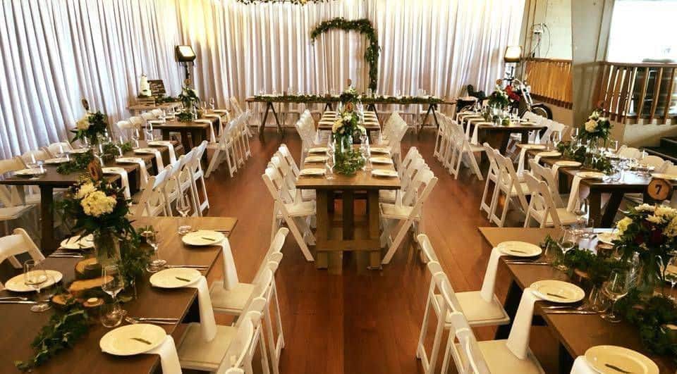 Elegant indoor event setup with wooden tables and white chairs, perfect for community gatherings at East End Surf Life Saving Club.