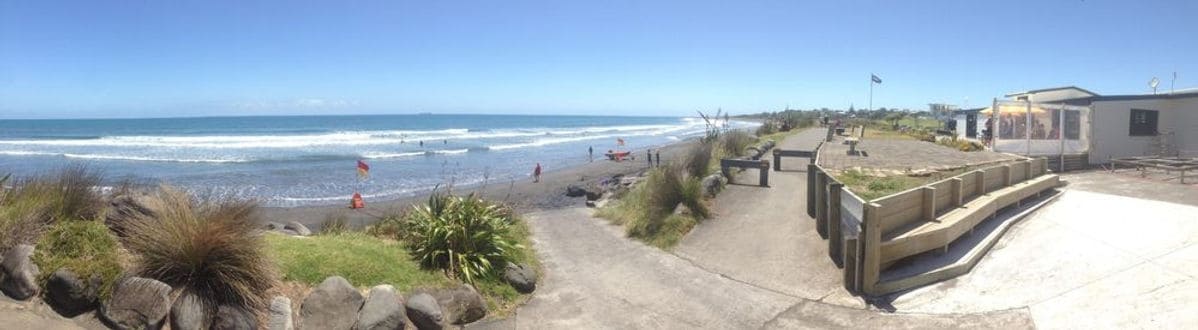 Sunny beach scene at East End Surf Life Saving Club, New Zealand, with surf, sand, and lifeguard facilities.