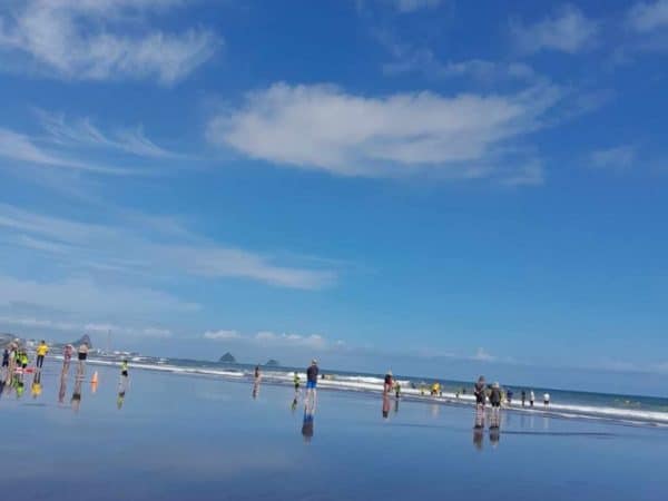 Bright yellow surf rescue boards on beach shore with people swimming and surfing in background, under a blue sky with clouds.