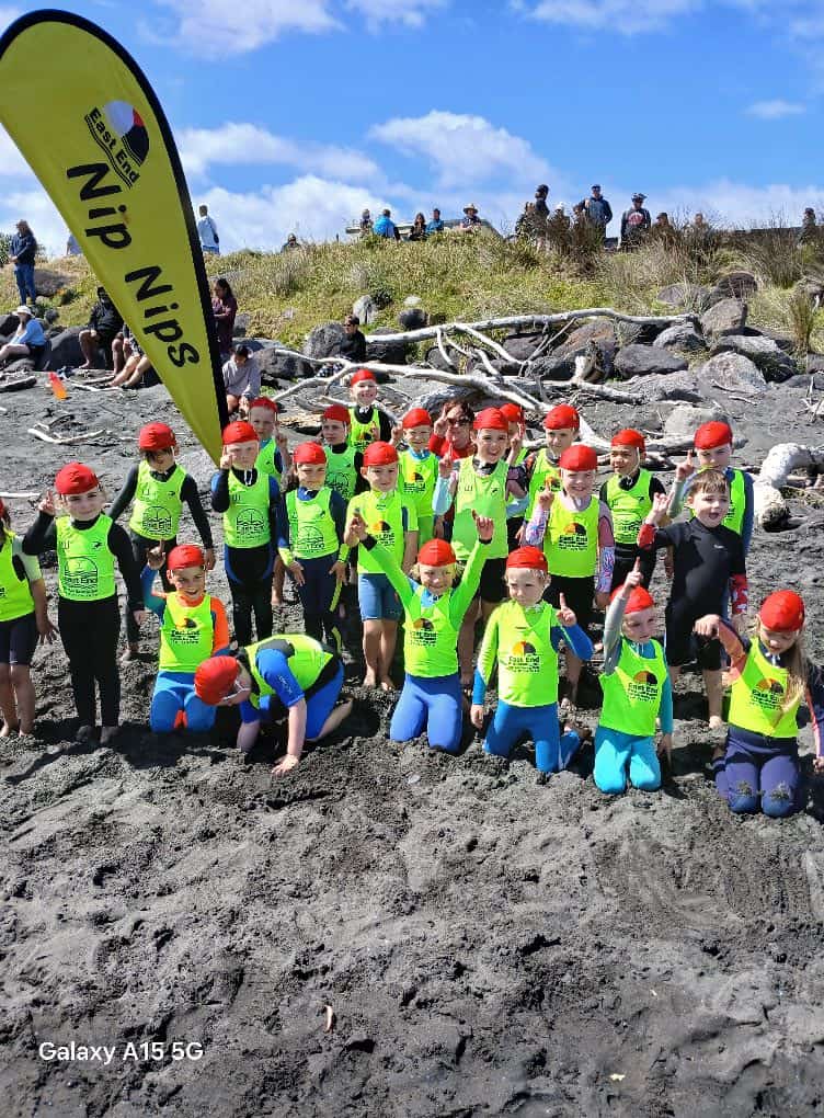 Young surf lifesavers in bright green vests and red hats at East End Surf Life Saving Club event on the beach.