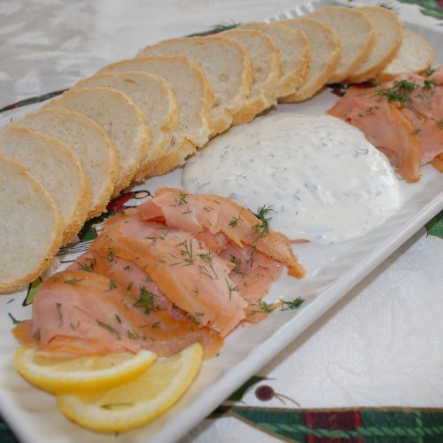 Smoked salmon with lemon slices, dill, and creamy sauce on a white platter.