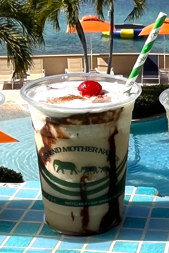 Scrubslide tropical cocktail on poolside with Scrub Island sign in background.
