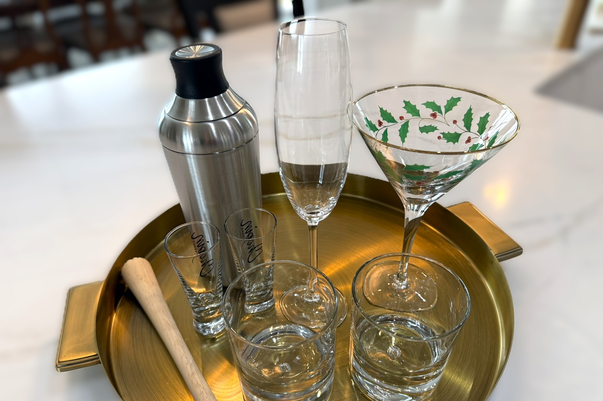 A stylish collection of cocktail glasses, shaker, and bar tools displayed on a gold tray for drinks and appetizers.