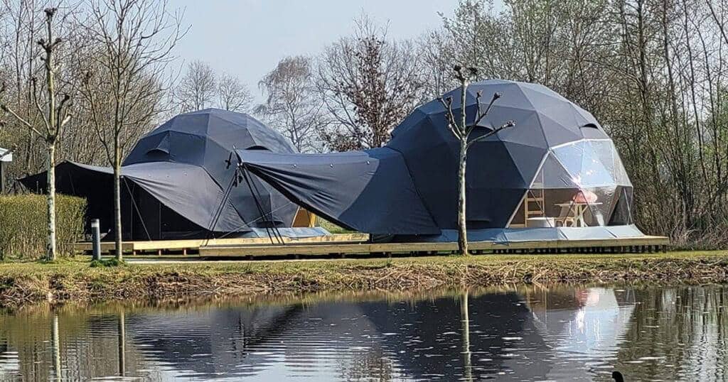 Unique geodesic dome tiny house designed by EJH Distribution for modern, eco-friendly living, featuring large glass windows and sustainable materials, situated by a tranquil lake for a nature-inspired lifestyle.