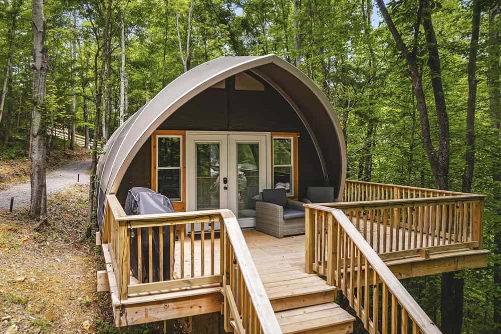 Secluded glamping cabin with wooden deck nestled in lush forest, perfect for outdoor retreat and relaxation.