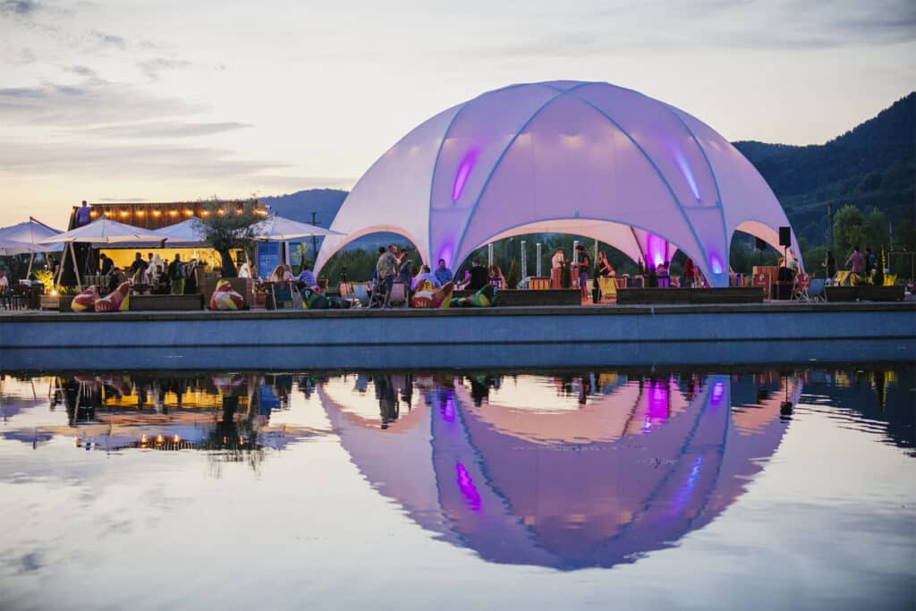 Modern outdoor event space with illuminated dome, lake reflection, and mountain scenery for events and entertainment.