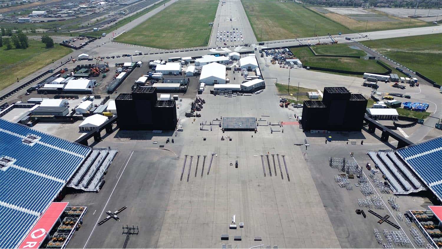 Loading and setup of event stage at EJH Distribution for outdoor concert or event in an open parking lot with equipment and tents.