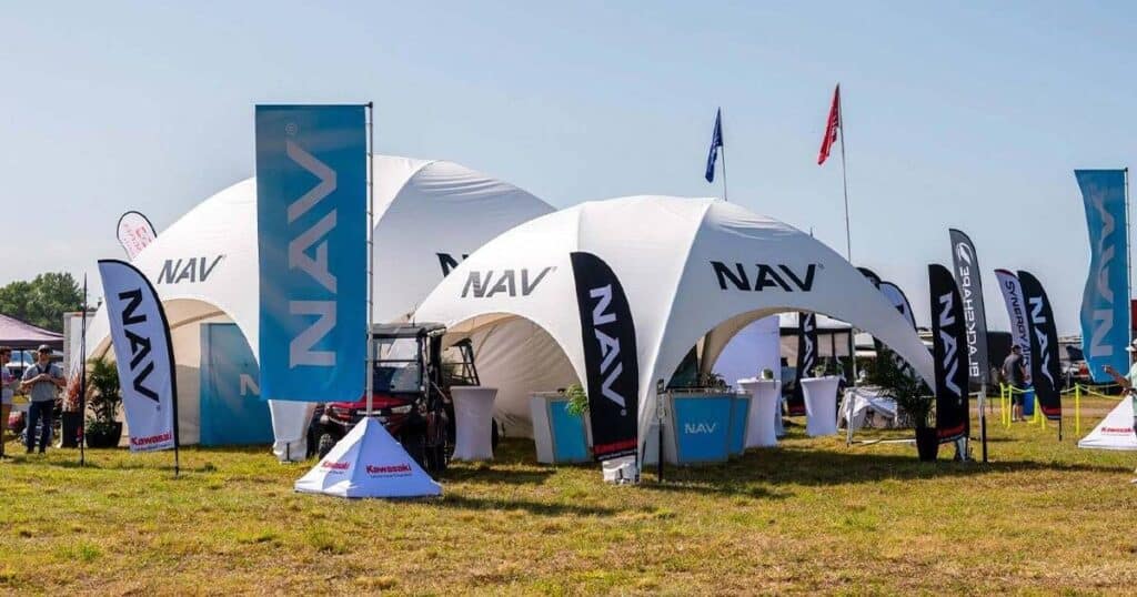 NAV motorcycle and watercraft dealer booth at outdoor expo, showcasing innovative products with branded tents, flags, and promotional displays.