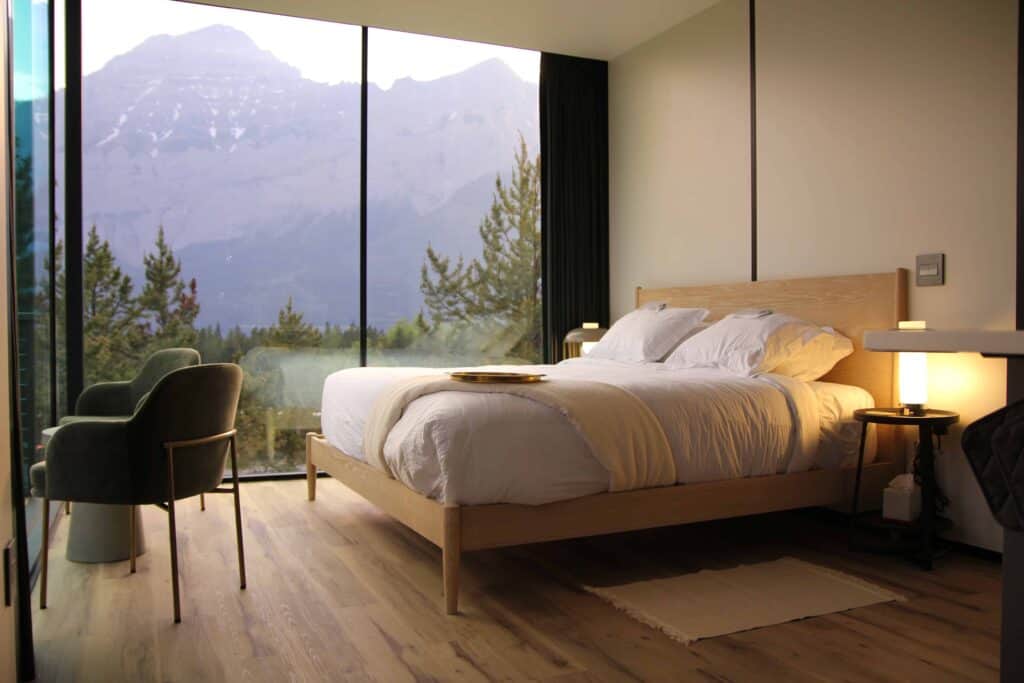Luxury hotel bedroom with mountain view, modern furnishings, and large floor-to-ceiling windows, showcasing contemporary design and scenic nature surroundings for a relaxing stay.