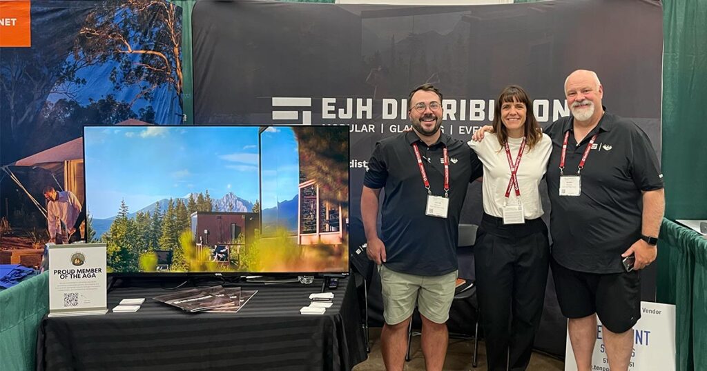 EJH Distribution booth at a trade show with representatives posing, showcasing large TVs, and promotional materials, emphasizing distribution and event services.