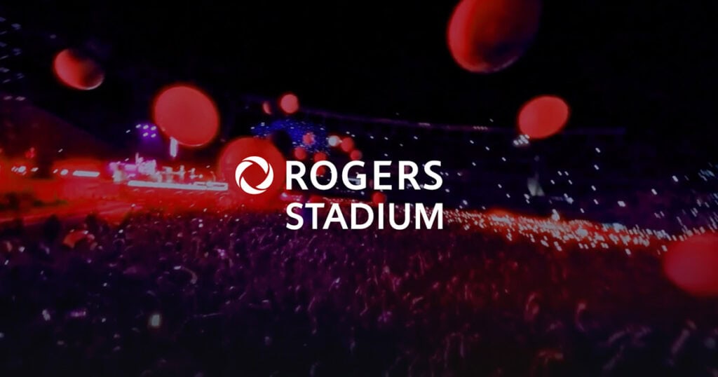 Red lights at Rogers Stadium during event, vibrant, illuminated atmosphere, lively crowd, entertainment, concert, sports, urban night scene, energy, large venue, nightlife, modern stadium, event preparation, atmosphere, excitement, venue lighting, concert lighting, entertainment event, stadium experience, nightlife scene, event promotional image, Rogers Stadium, concert or sports event.