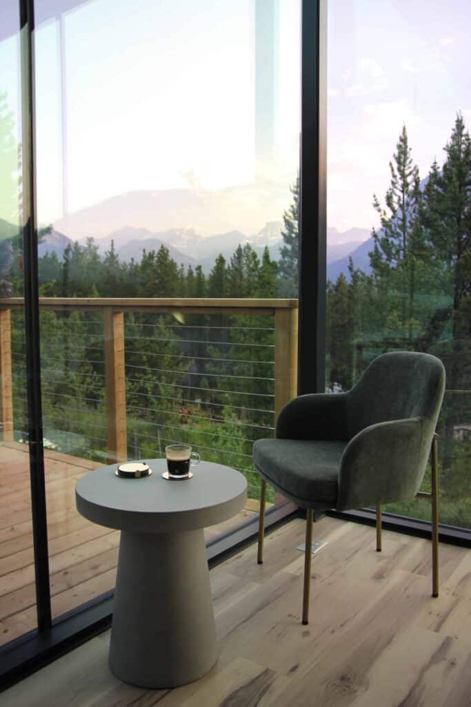 Modern living space with a cozy armchair and a scenic mountain view through large glass windows, perfect for relaxation and enjoying nature.