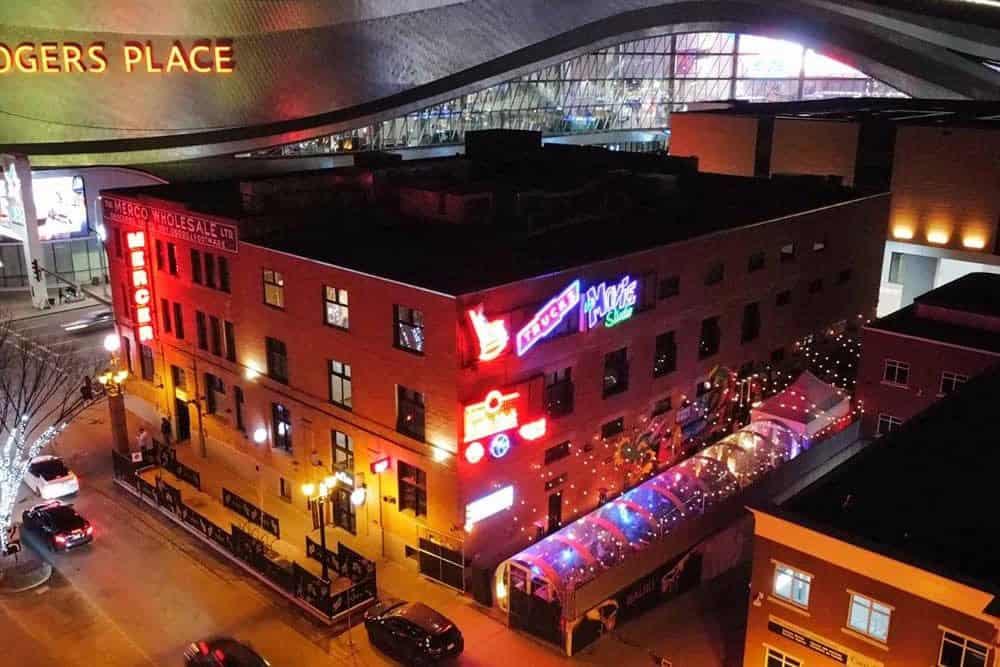Vibrant downtown nightlife scene with illuminated signage and outdoor seating at a trendy restaurant or bar, showcasing urban hospitality and entertainment in a lively city environment.