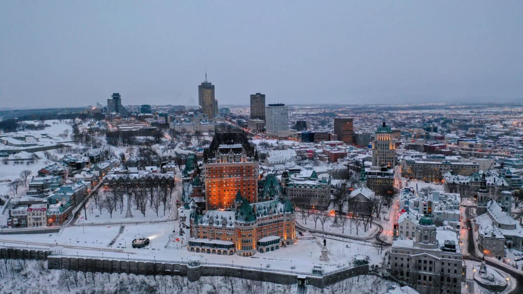 Aerial view of Quebec City covered in snow, showcasing historic Château Frontenac and modern downtown skyscrapers during winter, highlighting logistics and distribution potential in snowy climates.