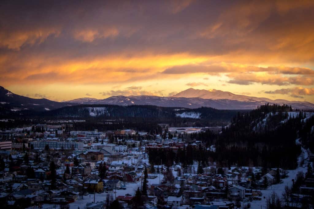 Snow-covered town in mountain valley at sunset with dramatic colorful sky and distant peaks, illustrating scenic winter landscape and outdoor beauty.