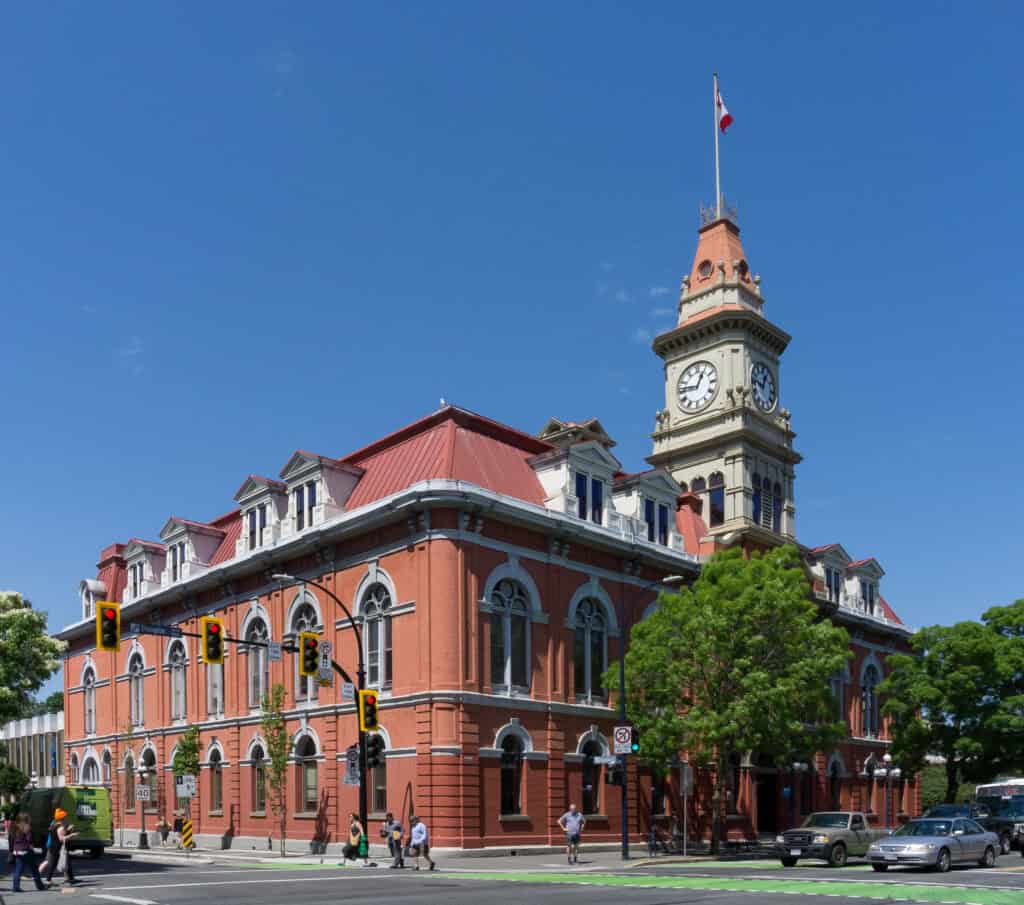 City hall building with clock tower in downtown with traffic and people, historical architecture and municipal government offices, sunny day with clear blue sky, EJH Distribution logo in image metadata.