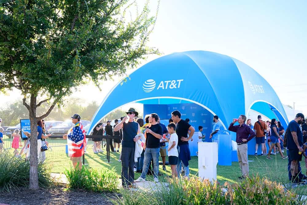 Bright blue AT&T branded event tent with people gathering, engaging, and enjoying at an outdoor promotional event under sunny weather.