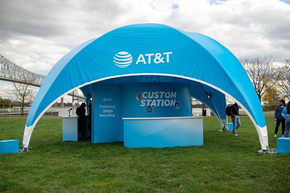 AT&T branded outdoor event booth at a public park with a blue tent and promotional display.