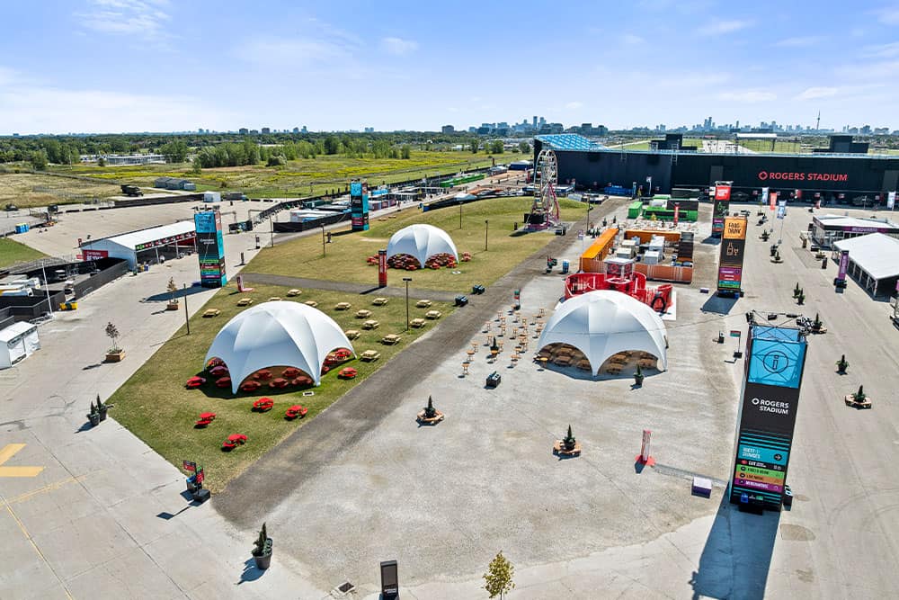 Aerial view of Rogers Stadium featuring oversized white tents, vendor booths, rides, and digital signage, set against a backdrop of city skyline and clear blue skies. Perfect for concerts, festivals, and outdoor events.