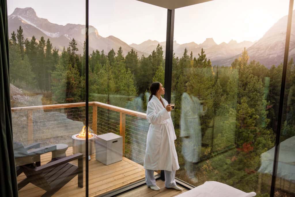 A woman in a white coat enjoying the scenic mountain view from a modern tiny home balcony.