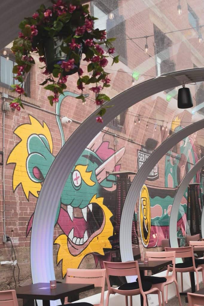 Bright outdoor seating area featuring a lively dragon mural, decorative arches, and hanging flower baskets, creating a welcoming atmosphere for dining in Canada.