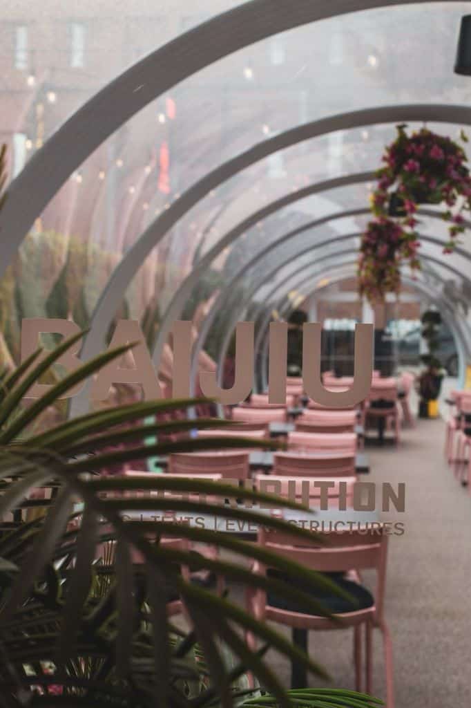 Charming outdoor patio featuring pink chairs, lush plants, and decorative arches, perfect for relaxing and enjoying the best patio experience in Canada at Baijiu.