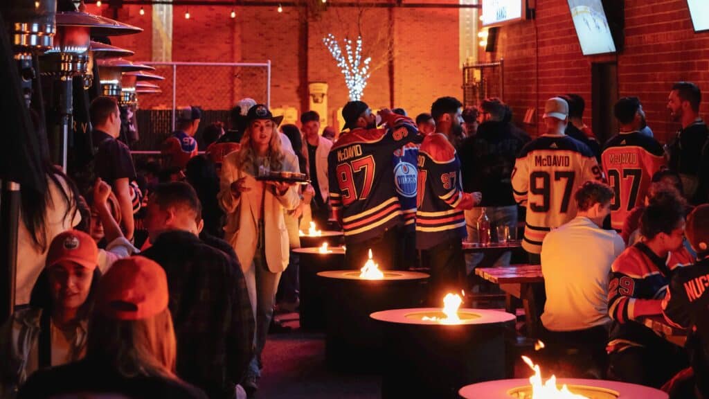 A lively patio scene at Baijiu, Canada’s best patio, featuring groups of friends enjoying drinks and socializing around fire pits in a vibrant, warm atmosphere.