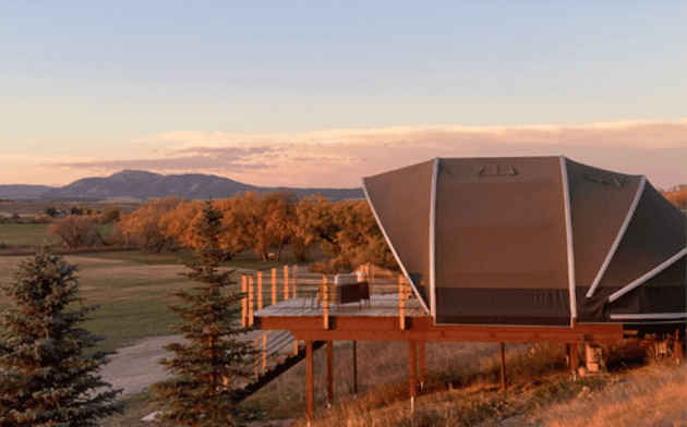 Spacious open-air pavilion with unique architectural design overlooking a picturesque landscape during sunset, surrounded by trees and open fields, ideal for outdoor gatherings and events.