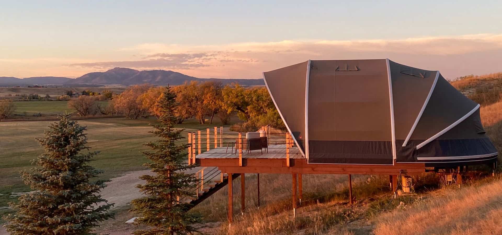 Observatory with a sleek, contemporary design situated on a grassy hilltop, offering panoramic views of the surrounding countryside and mountains during sunset.