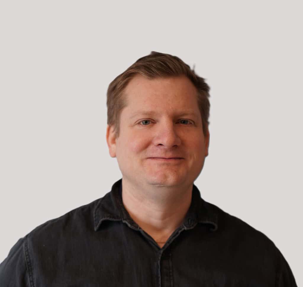 A man in a black shirt smiling for the camera.