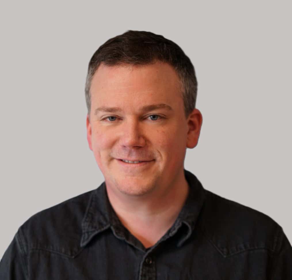 A man in a black shirt smiling for the camera.