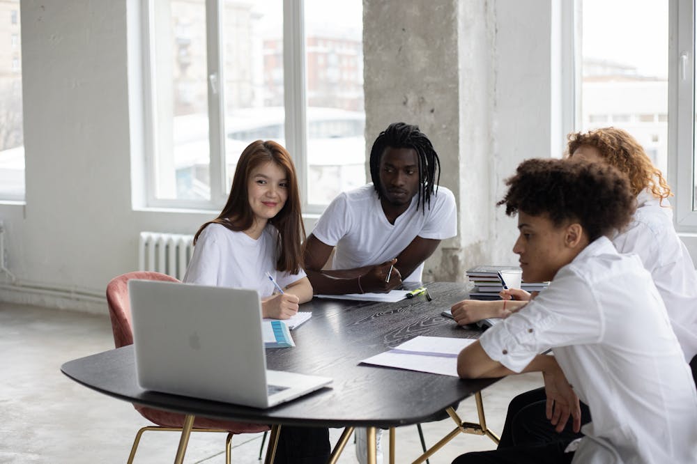 Pessoas reunidas em torno de mesa de cor preta, conversando enquanto observam notebook. Ilustração do texto sobre taxa de marketing de franquias.
