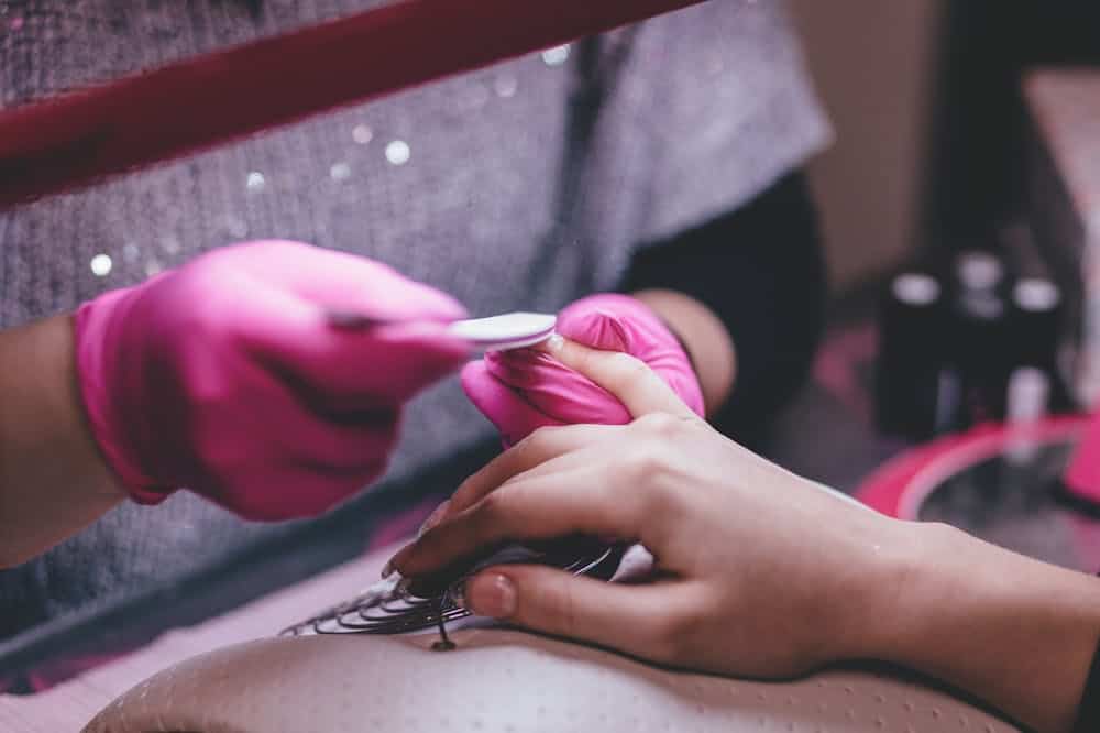 Manicure usando luva rosa, enquanto faz unhas de cliente. Ilustração do texto sobre franquias de manicure e pedicure express.