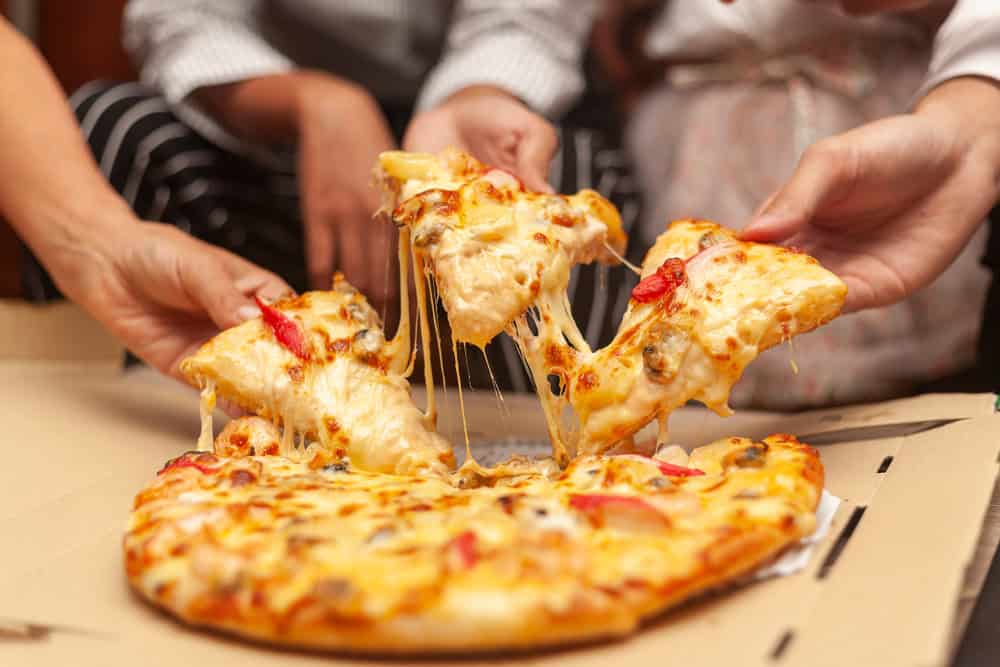 9 MELHORES IDEIAS de negócios em alta que tendem a crescer Negócios em alta: amigos pegando pedaço de pizza durante uma reunião