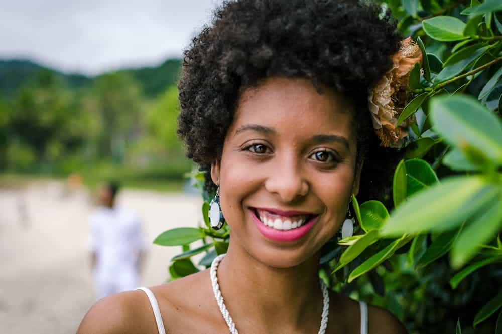 Mulher com belo sorriso, próxima de uma cerca viva de folhas verdes. Ilustração do texto sobre franquias no nordeste.
