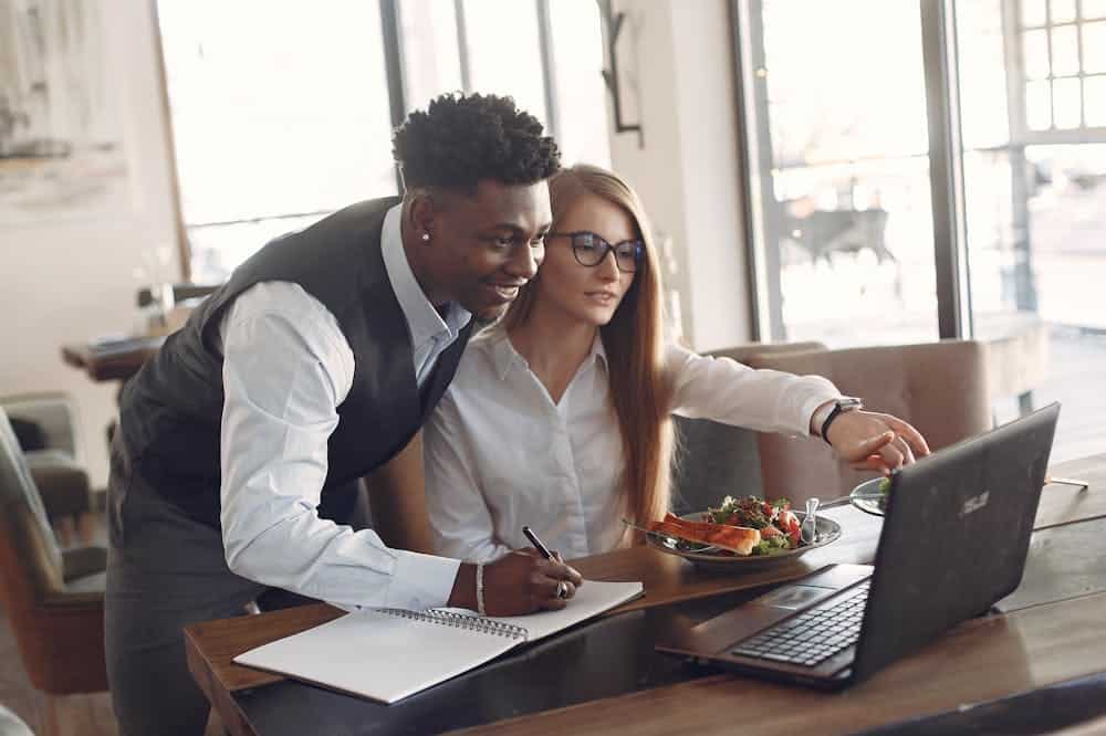 Homem e mulher sorridentes, analisando computador cinza. Ilustração do texto sobre ABF franquias.