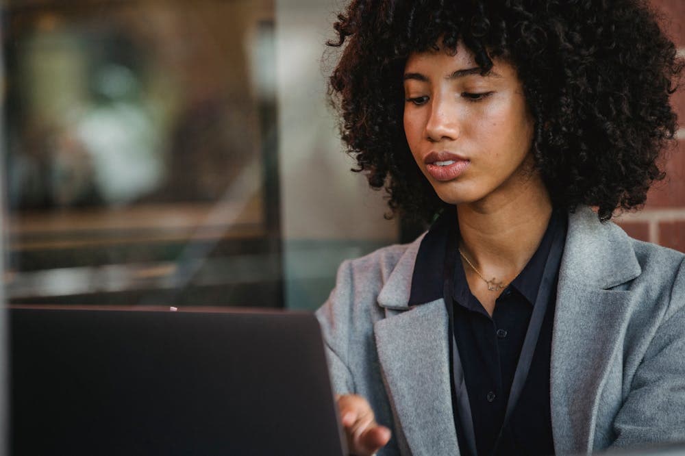 Mulher usando paletó cinza, trabalhando em notebook. Ilustração do texto sobre negócios para 2021.