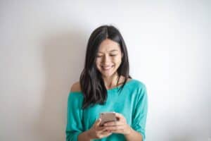 Mulher sorridente, usando blusa azul, enquanto usa o celular. Ilustração do texto sobre franquia unitária.