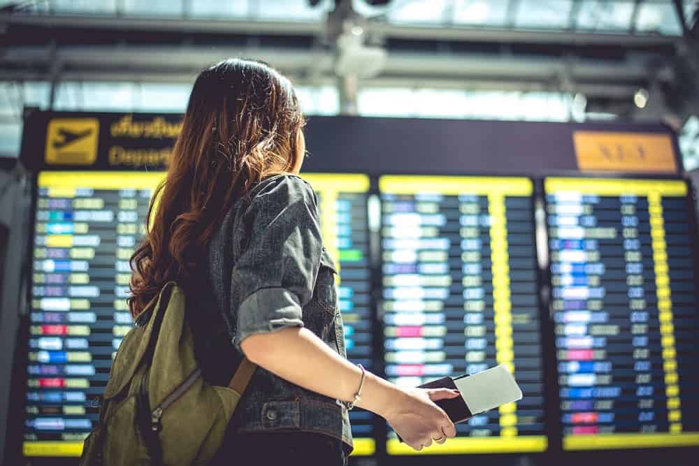 Mulher usando mochila verde, observa o quadro com informações de embarque. Ilustração do texto sobre franqueados Encontre Sua Viagem.