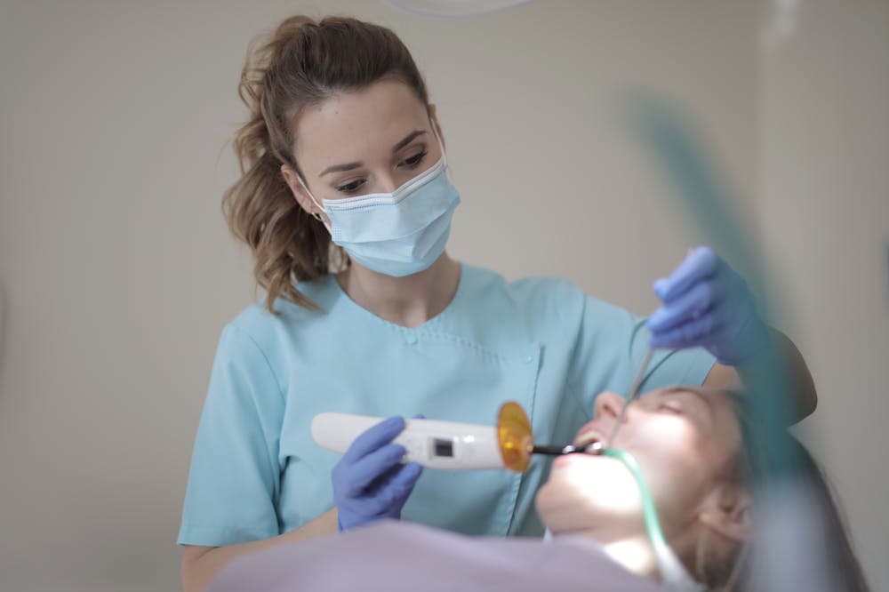 Dentista usando máscara e uniforme azul, fazendo procedimento na boca de um paciente. Ilustração do texto sobre franquia Odontocompany.