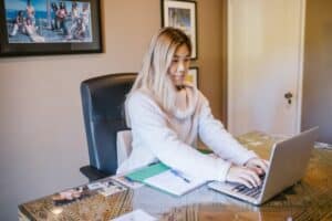 Mulher atenta, trabalhando em frente ao notebook, enquanto está sentada em uma mesa de escritório marrom. Ilustração do texto sobre empreendedorismo na pandemia.